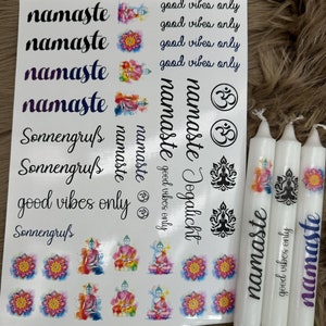 May include: A selection of white candles and sticker sheets with spiritual and yoga-themed designs. The stickers feature the word "namaste", lotus flowers, and Buddha illustrations. The candles are decorated with similar imagery and the words "good vibes only".