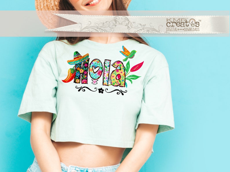 May include: A light mint green short-sleeved crop top featuring a colorful graphic print of the word Hola. The letters are filled with floral patterns and accompanied by a small sombrero, a chili pepper, a bird, and decorative black swirls.