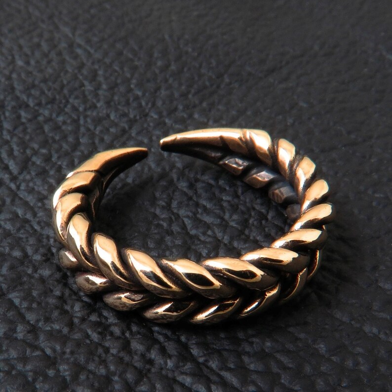May include: A gold-toned ring with a braided design. The ring is open and has a pointed end.