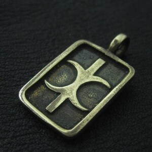 May include: A rectangular pendant with a stylized symbol in a bronze finish. The symbol features a central vertical line intersected by two curved lines, all within a raised border. The pendant has a loop for a chain.