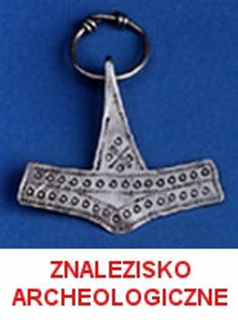May include: A silver-colored pendant in the shape of a hammer, attached to a metal ring. The hammer has a detailed design with small circular and cross-shaped patterns. The text "ZNALEZISKO ARCHEOLOGICZNE" is displayed in red at the bottom.