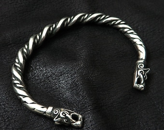 May include: A silver cuff bracelet featuring a twisted rope pattern. The bracelet has decorative animal head terminals. The open ends of the bracelet are designed to fit around the wrist. The bracelet is displayed on a black surface.