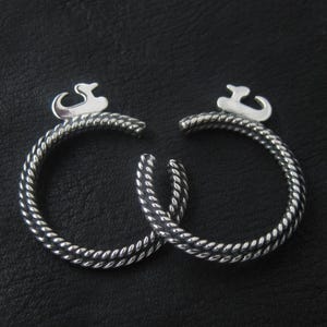 Op de afbeelding: Twee zilveren ringen met een gedraaid touwontwerp en een klein eendje-bedeltje aan elke ring.