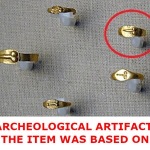 May include: A collection of gold rings, each with a unique design, presented on white supports against a textured backdrop. The rings are likely antique or vintage, highlighting their historical value. The text at the bottom reads: ARCHEOLOGICAL ARTIFACT, THE ITEM WAS BASED ON.