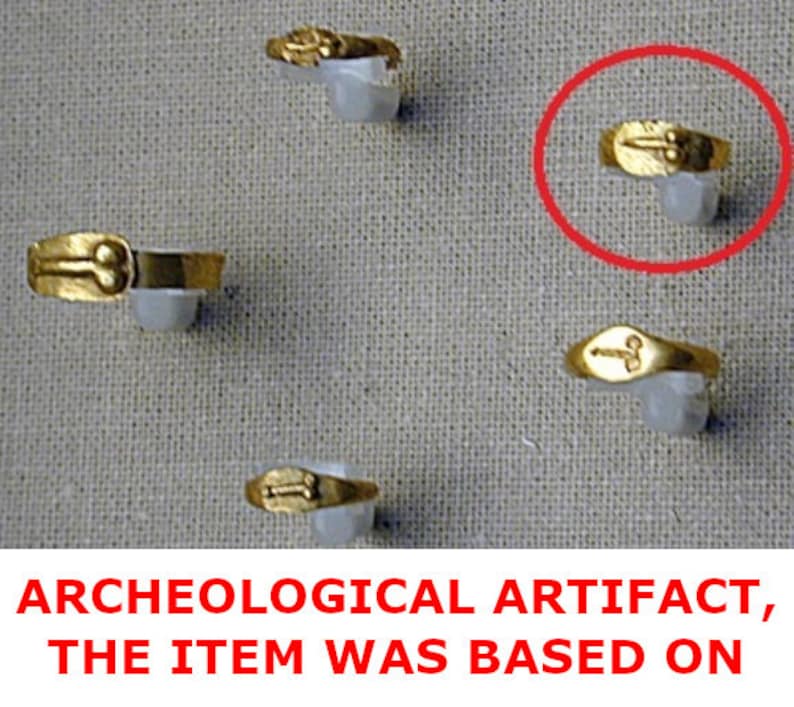 May include: A collection of gold rings, each with a unique design, presented on white supports against a textured backdrop. The rings are likely antique or vintage, highlighting their historical value. The text at the bottom reads: ARCHEOLOGICAL ARTIFACT, THE ITEM WAS BASED ON.