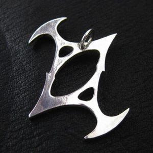 May include: A silver pendant with an unusual, abstract design. The pendant has a central oval shape with three smaller oval cutouts and sharp, curved edges. A small loop is at the top for a chain. The pendant is shown against a dark background.
