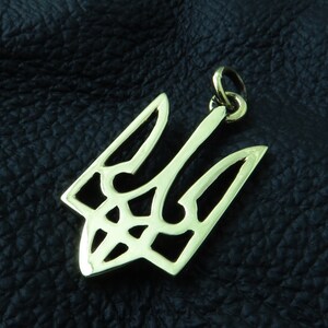 May include: A gold-colored metal pendant in the shape of a trident, a traditional Ukrainian symbol. The pendant has a detailed, intricate design and a loop at the top for attaching to a chain.