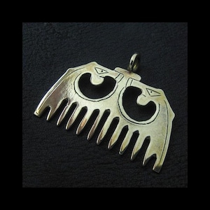 May include: A silver-colored pendant in the shape of a comb. The pendant features an openwork design with two stylized bird-like figures. The comb's teeth are visible at the bottom, and a loop is at the top for a chain.