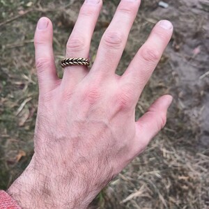 May include: A gold braided ring worn on the ring finger of a hand.