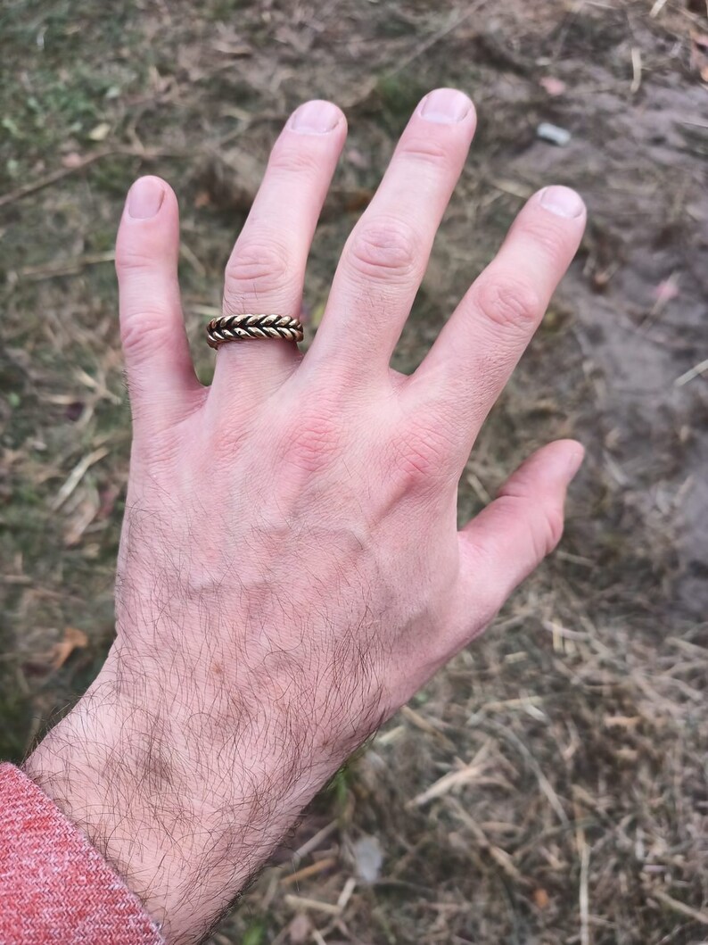 May include: A gold braided ring worn on the ring finger of a hand.