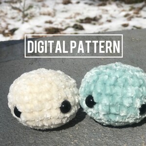Könnte beinhalten: Zwei gehäkelte Plüschtiere, eines weiß und eines hellblau, mit schwarzen Knopfaugen. Die Spielzeuge sind in Form von kleinen, runden Kreaturen. Der Text "DIGITAL PATTERN" wird über den Spielzeugen angezeigt.