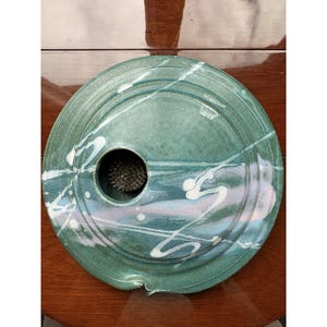 Peut inclure: Un crapaud de fleur rond en céramique de couleur sarcelle avec un motif de peinture blanche éclaboussée. Le crapaud a un trou central avec un porte-épingles en métal pour arranger les fleurs. L'objet est décoratif pour les compositions florales.