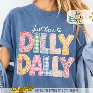 Op de afbeelding: Een blauw t-shirt met de tekst "Just here to DILLY DALLY" in kleurrijke letters in patchwork-stijl. Het ontwerp bevat bloemen-, ruit- en kanten patronen. Het shirt heeft ook de tekst "Certified Cool Designer" en "100% MY ORIGINAL IDEA".