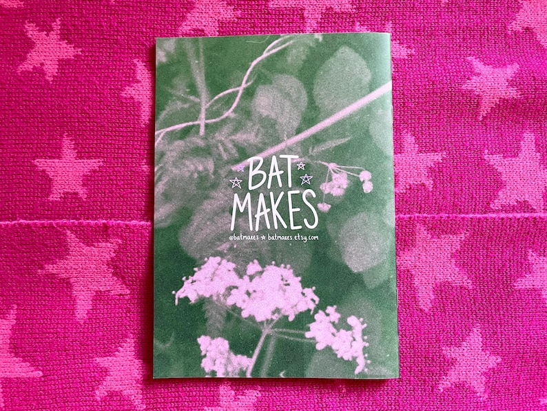 Puede incluir: Una tarjeta verde con el texto "BAT MAKES" en blanco, con un dise&ntilde;o floral. La tarjeta est&aacute; colocada sobre un fondo rosa con un patr&oacute;n de estrellas. Tambi&eacute;n se ve la direcci&oacute;n del sitio web.