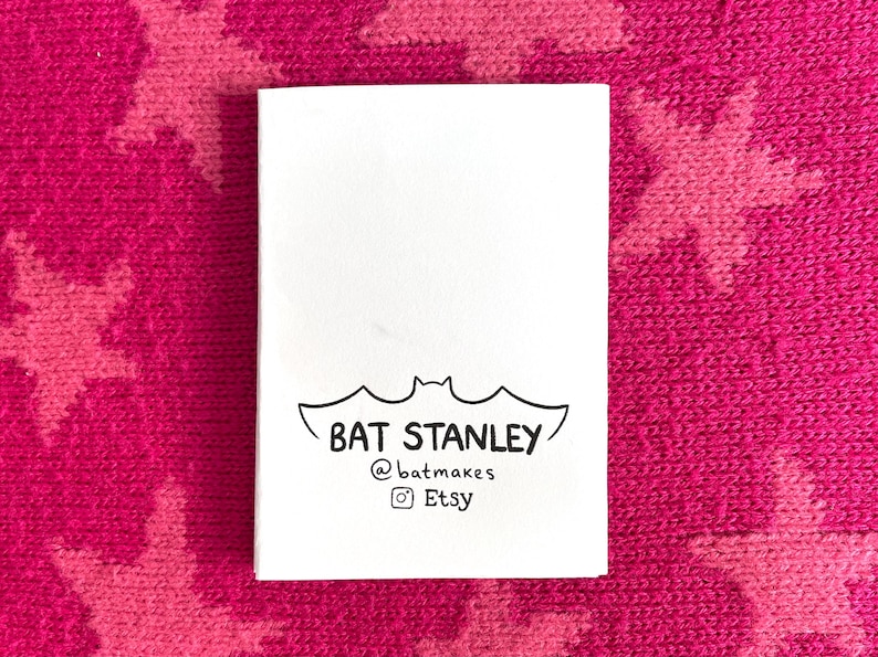 Peut inclure: Une carte blanche avec une illustration de chauve-souris noire et le texte "BAT STANLEY @batmakes Etsy" est pr&eacute;sent&eacute;e sur un fond rose avec un motif d'&eacute;toiles. La carte est rectangulaire et le texte est centr&eacute;.