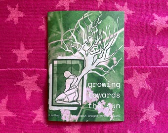 May include: A book cover with the title "growing towards the sun" and an illustration of a person and a tree. The cover is green with white text and a white tree illustration. The background is a pink fabric with star patterns.