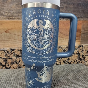 May include: A blue stainless steel travel mug with a white lid and a black handle. The mug features a silver design of a dragon with wings and a quote that reads "There's nowhere in existence you could that I wouldn't find you. Violence" and "I have a thing for HIGHLORDS WINGLEADERS & FAE PRINCES".