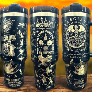 May include: Black stainless steel tumbler with a gold design featuring dragons, a castle, and the text "I am the sky and the power of every storm that has been. I am infinite."  The tumbler has a black handle and a black lid.