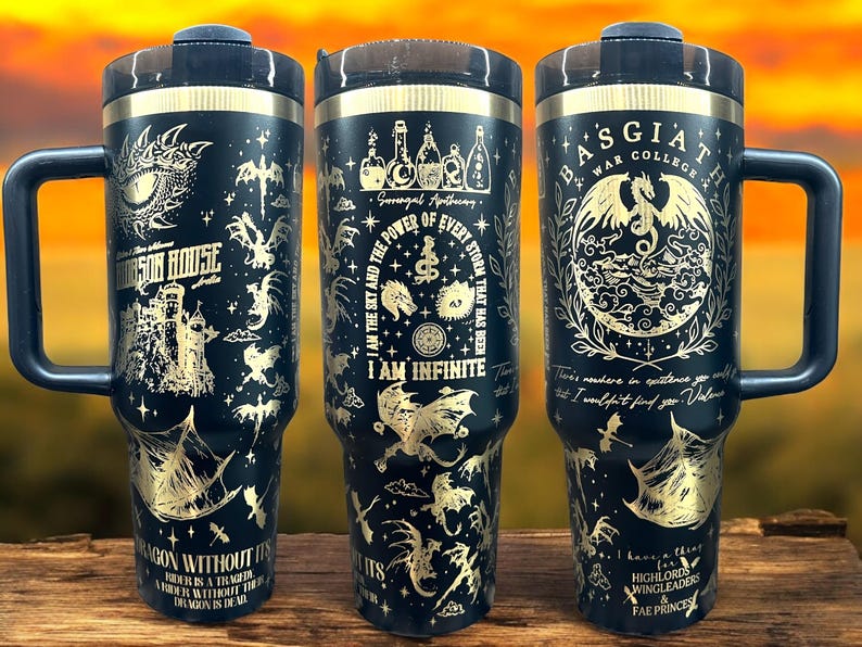 May include: Black stainless steel tumbler with a gold design featuring dragons, a castle, and the text "I am the sky and the power of every storm that has been. I am infinite."  The tumbler has a black handle and a black lid.