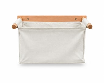 May include: A wall-mounted storage organizer featuring a rectangular light beige fabric pouch suspended from a horizontal wooden bar. The fabric is attached to two cylindrical wooden dowels on either side, which are connected to a flat wooden backboard.