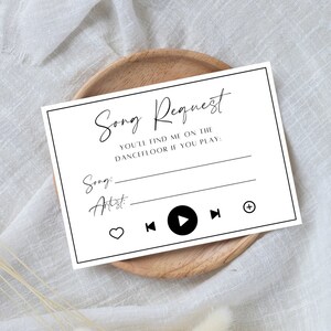 May include: A white song request card with black text, including the words "Song Request" and prompts for song and artist. The card features music player icons and the phrase "You'll find me on the dancefloor if you play:" on a wooden plate.