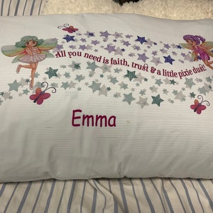 May include: White pillowcase with a pink and green fairy design. The pillowcase has a quote that reads "All you need is faith, trust & a little pixie dust!" and the name "Emma" is embroidered in pink.