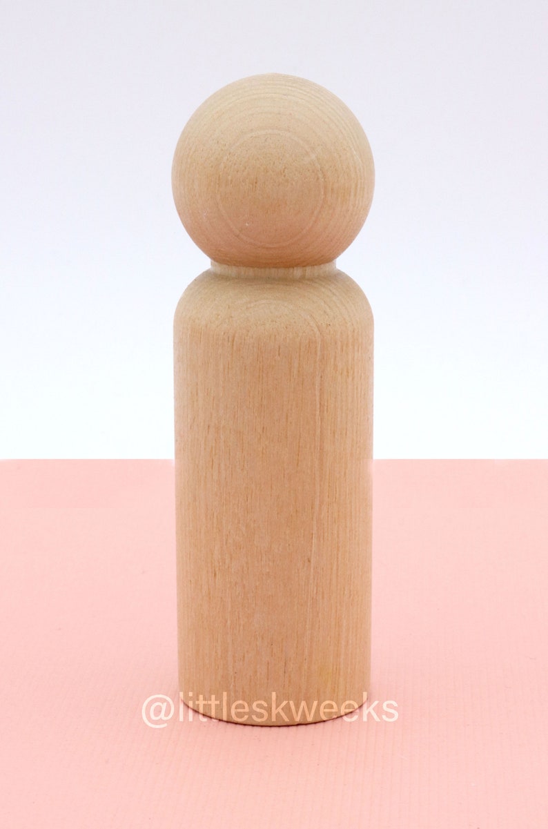 Op de afbeelding: Een houten pop met een rond hoofd en een cilindrisch lichaam. De pop is ongeverfd en heeft een natuurlijke houten afwerking.