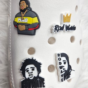 May include: Four black and white Rod Wave shoe charms. One charm features a cartoon image of Rod Wave with the text "Rod Wave" below. Another charm features a cartoon image of Rod Wave with the text "Rod Wave" below. The third charm features a cartoon image of Rod Wave with the text "Rod Wave" below. The fourth charm features a cartoon image of Rod Wave with the text "Rod Wave" below.