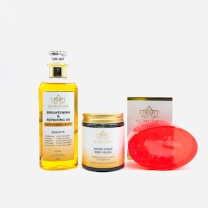 May include: A selection of skincare items, featuring a bottle of brightening oil, a jar of brown sugar body polish, a red soap bar, and a box. The oil bottle is yellow with a gold cap and a label that reads "Brightening & Repairing Oil". The body polish jar has a gold lid.