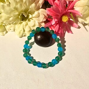 May include: A green and blue beaded bracelet with silver accents. The bracelet is made of round beads and is strung on a silver cord.