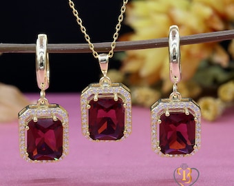 May include: A gold necklace, earrings, and pendant set with a large, dark red, square-shaped gemstone surrounded by smaller, clear gemstones.