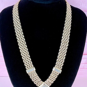Peut inclure: Un collier en métal doré composé d'une large chaîne en maille tressée avec trois accents carrés incrustés de petits cristaux clairs, accompagné d'une paire de boucles d'oreilles assorties de forme carrée avec un pavé de cristaux central.