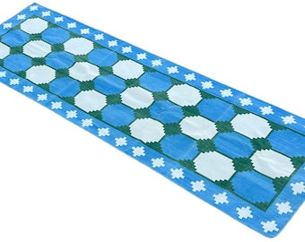 Op de afbeelding: Een blauwe en witte loper met een geometrisch patroon. De loper heeft een groene rand met witte sterren.