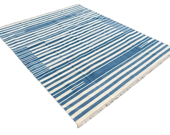 May include: A blue and white striped rug with a fringe border. The rug has a contemporary design with a subtle pattern.