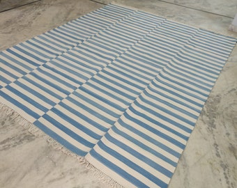May include: A blue and white striped rug with a fringe border. The rug is made of cotton and is perfect for adding a touch of color and style to any room.