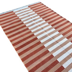 K&ouml;nnte beinhalten: Ein gestreifter Teppich mit abwechselnd roten und wei&szlig;en Streifen. Die Streifen sind diagonal angeordnet und bilden ein geometrisches Muster.