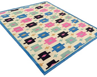 May include: A cream-colored rug with a geometric pattern in shades of blue, pink, black, and green. The rug has a blue border.