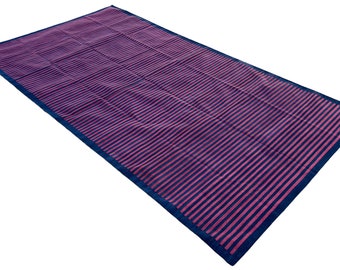 Op de afbeelding: Een gestreept picknickkleed in roze en marineblauw. Het kleed is gevouwen en ligt op een witte achtergrond.