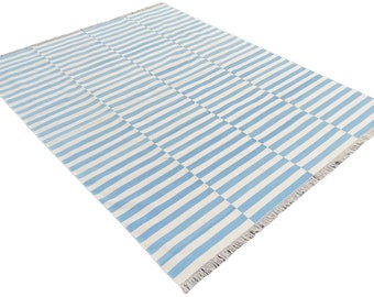 May include: A rectangular rug with a blue and white striped pattern. The stripes alternate in direction, creating a checkered effect. The rug has a fringed edge and is suitable for indoor use.