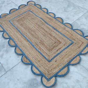 Op de afbeelding: Een rechthoekig jute vloerkleed met een blauwe rand en gegolfde randen. Het vloerkleed heeft een natuurlijke, aardse tint en is perfect om elke kamer een vleugje rustieke charme te geven.