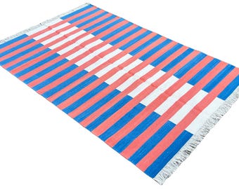 Op de afbeelding: Een rechthoekig tapijt met een gestreept patroon in koraal, wit en blauw. Het tapijt heeft een gefranjerde rand en is geschikt voor gebruik binnenshuis. De strepen lopen in de lengte over het tapijt.