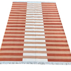 K&ouml;nnte beinhalten: Ein gestreifter Teppich mit abwechselnden B&auml;ndern in Orange und Wei&szlig;. Der Teppich hat einen Fransenrand.