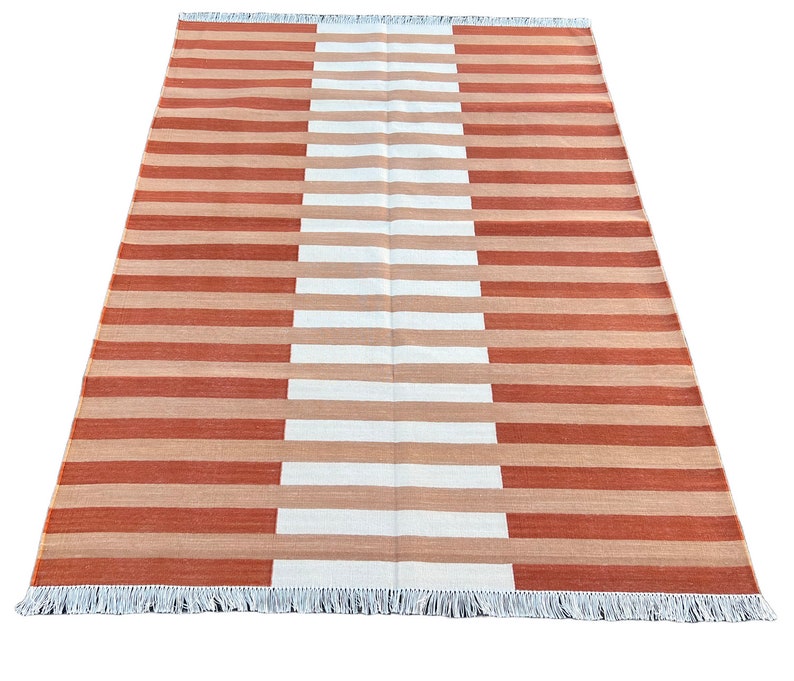 K&ouml;nnte beinhalten: Ein gestreifter Teppich mit abwechselnden B&auml;ndern in Orange und Wei&szlig;. Der Teppich hat einen Fransenrand.