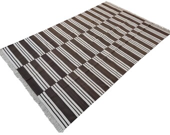 Puede incluir: Una alfombra de rayas marrones y blancas con flecos en todos los lados. La alfombra está hecha de algodón y es perfecta para añadir un toque de estilo a cualquier habitación.