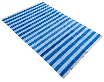 Op de afbeelding: Een blauw en wit gestreept tapijt met franjes aan alle kanten. Het tapijt is gemaakt van een zacht, geweven materiaal.
