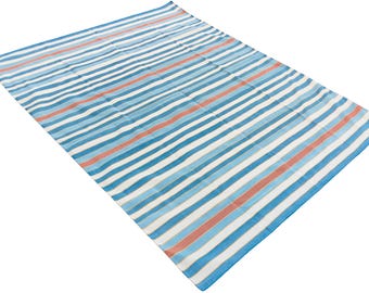 Op de afbeelding: Een rechthoekige strandlaken met strepen. De strepen wisselen af tussen blauwe, witte en koraal-oranje tinten. De deken is gemaakt van een lichte stof, geschikt voor gebruik buitenshuis.