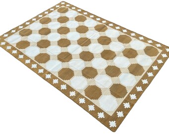 Op de afbeelding: Een bruin en wit geometrisch patroon tapijt met een witte rand met een herhalend stervormig ontwerp.