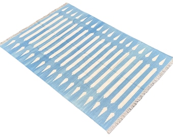 Peut inclure: Tapis rectangulaire bleu et blanc à motifs rayés. Le tapis présente des rayures blanches larges alternant avec un fond bleu clair. Les bords sont ornés de franges. Convient pour un salon ou une chambre.