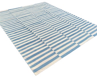 May include: A blue and white striped rug with a woven texture. The rug is folded in half and laid out on a white background.