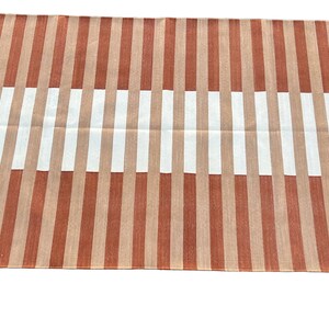 K&ouml;nnte beinhalten: Ein gestreifter Teppich mit abwechselnden B&auml;ndern in Orange und Wei&szlig;. Der Teppich hat einen Fransenrand.